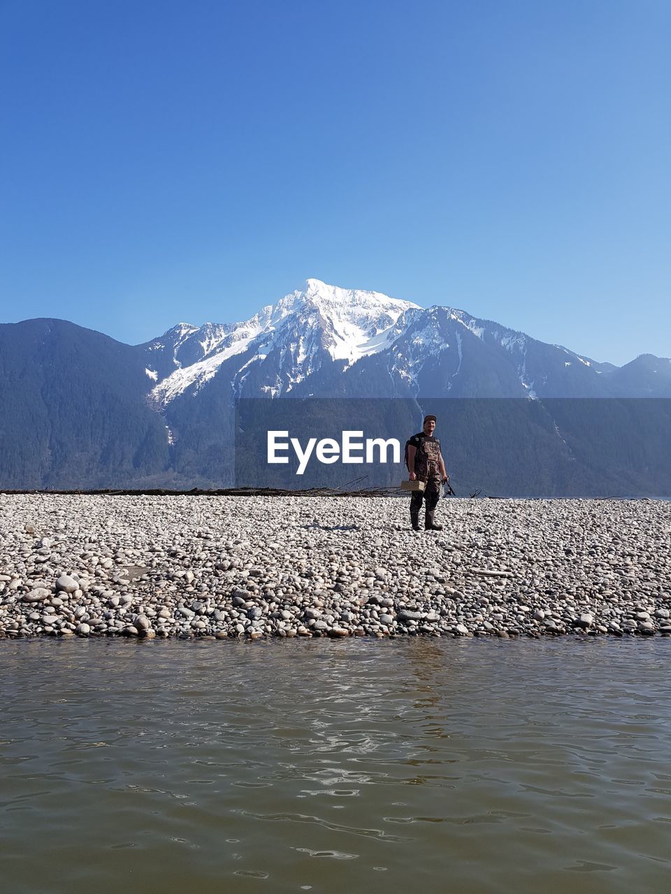 Fishing man on snowcapped mountain against blue sky