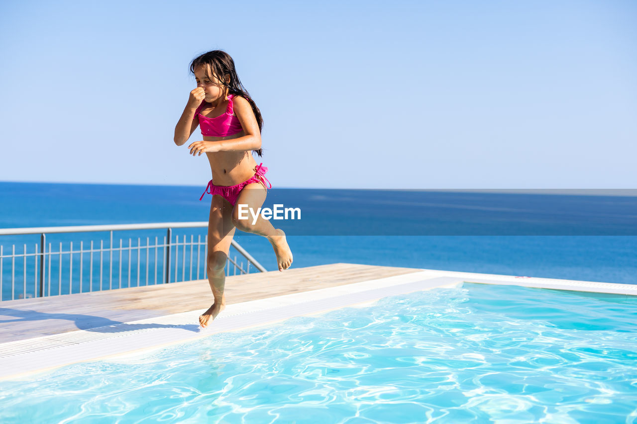 Funny little girl have a fun with a splash near swimming pool