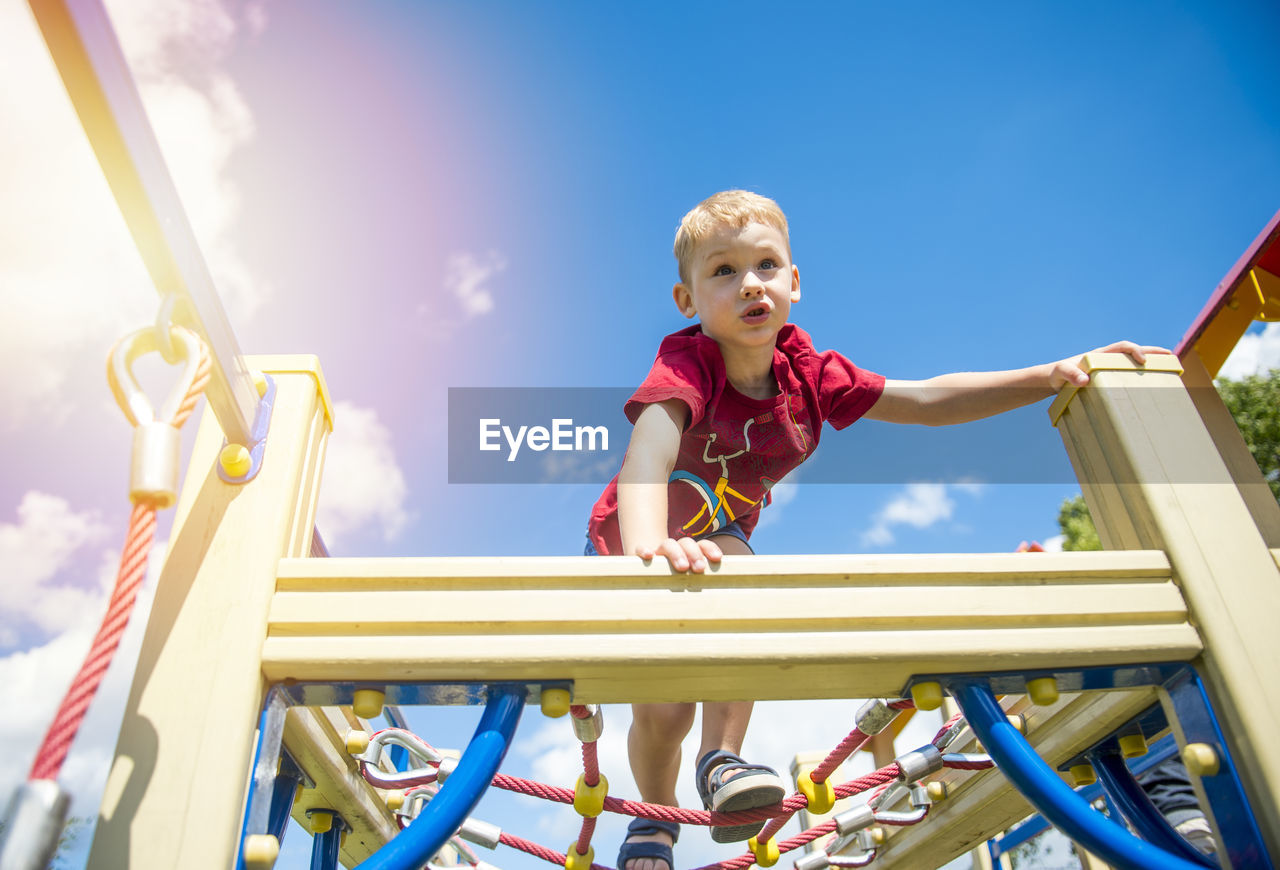 Low angle view of boy playing on jungle gym in playground