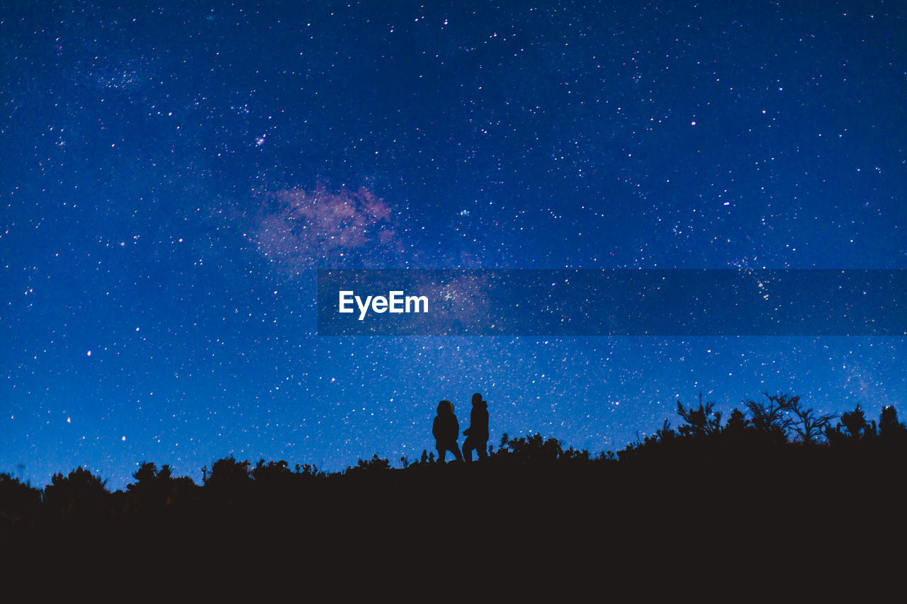 Low angle view of silhouette people standing on mountain against star field at night