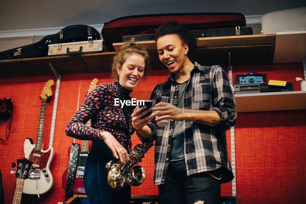 Woman with saxophone looking at man using smart phone while practicing at recording studio