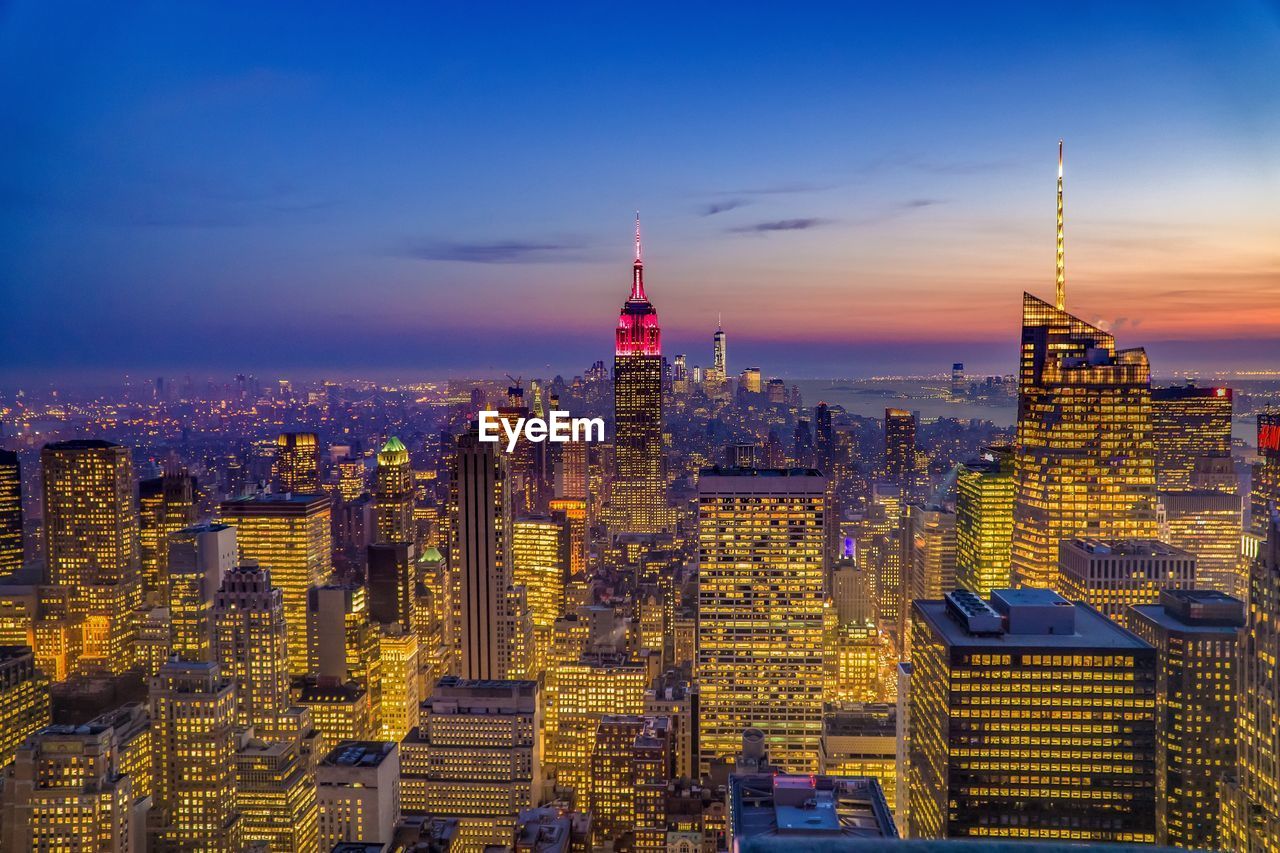 Illuminated empire state building amidst buildings at manhattan