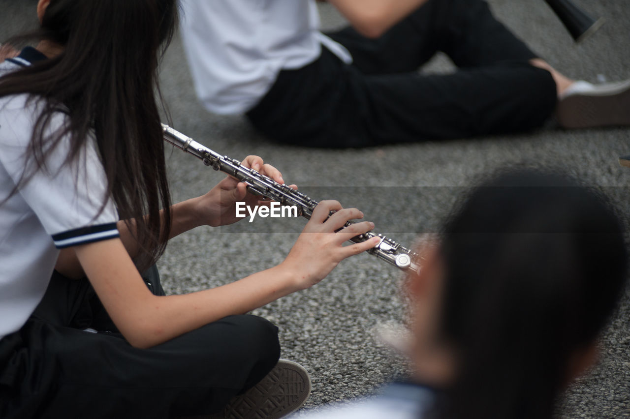 School girls playing flutes while sitting on footpath