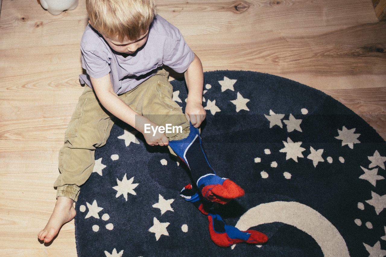 High angle view of boy wearing socks while sitting on carpet at home