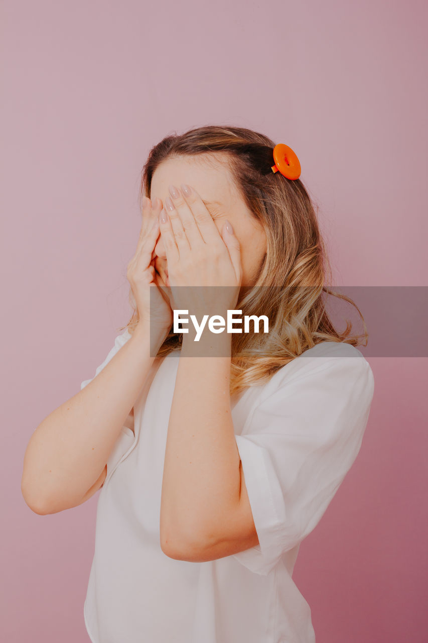 MIDSECTION OF WOMAN STANDING AGAINST WALL WITH PINK BACKGROUND