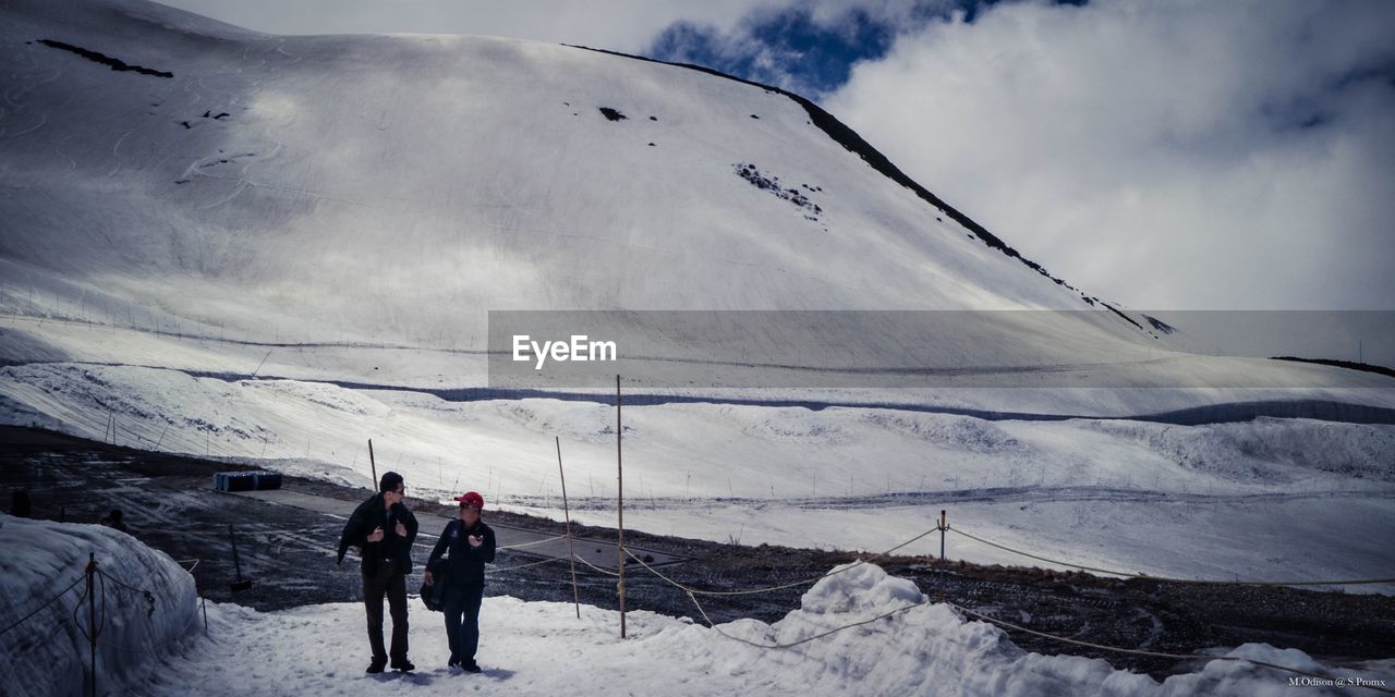 PEOPLE WALKING ON SNOWCAPPED MOUNTAINS AGAINST SKY