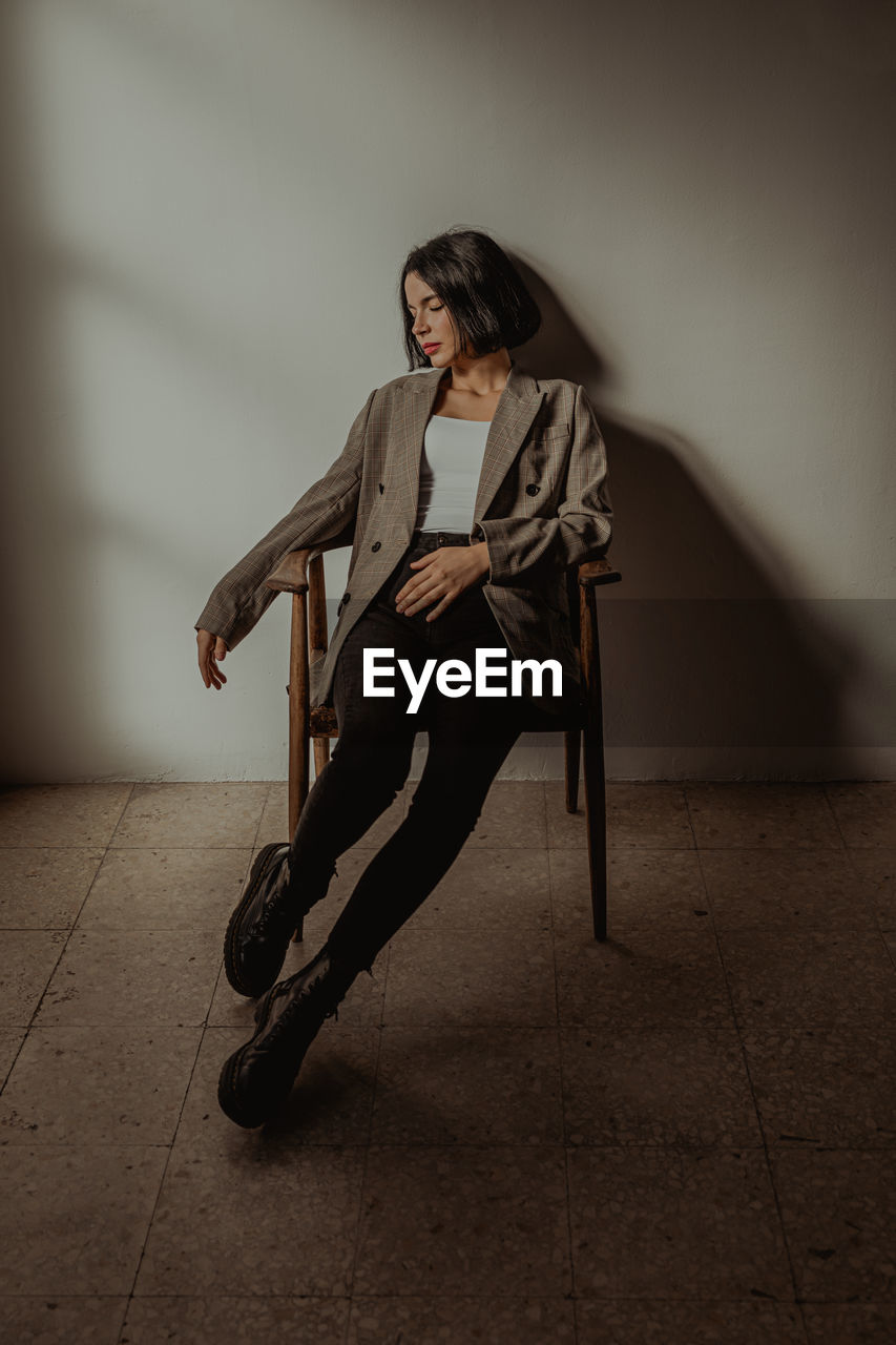 Relaxed female wearing trendy clothes sitting on chair while touching hair with closed eyes