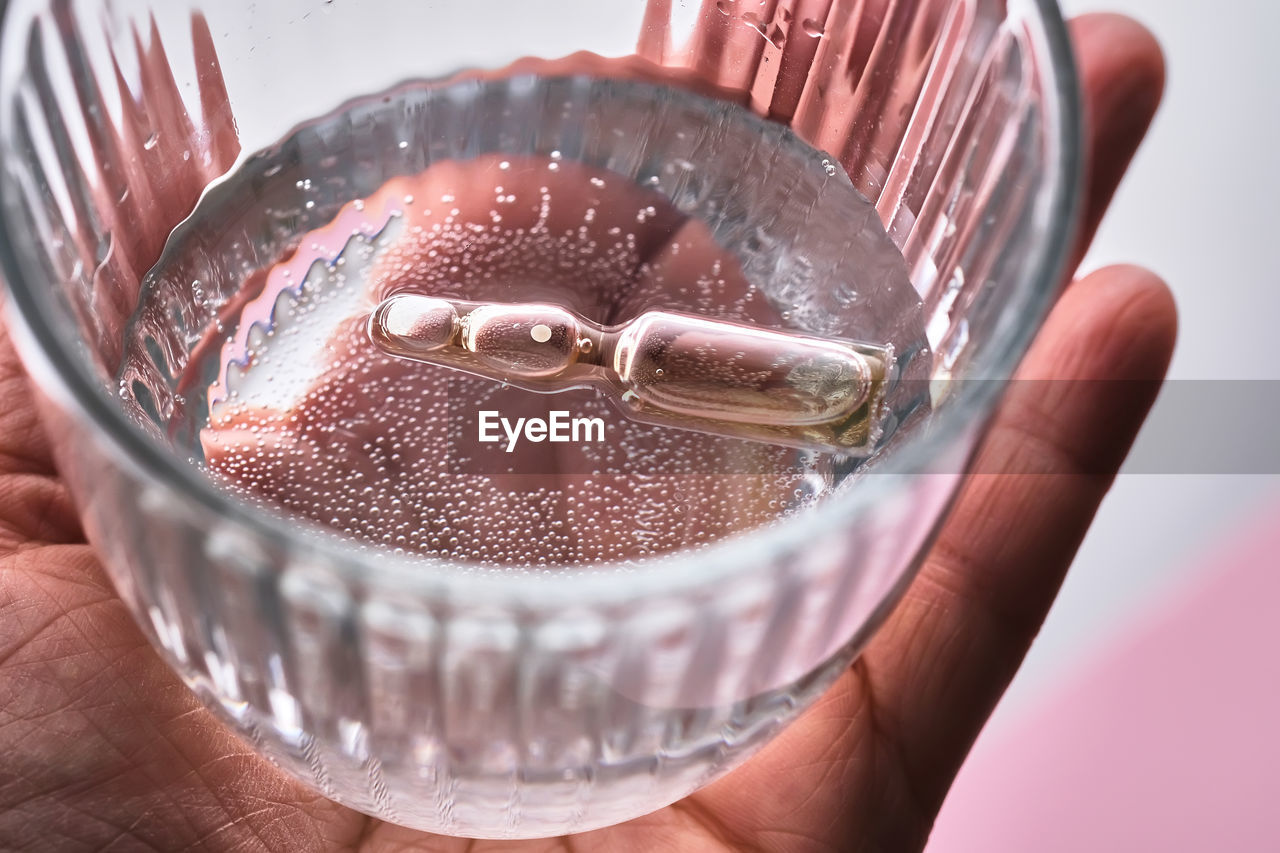 Ampoule in a mug with water on a pink background. the symbol of humidification.
