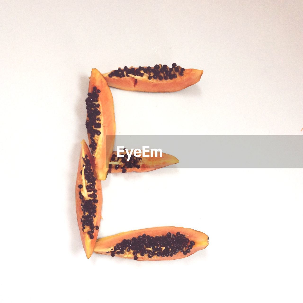 Papaya slices arranged in letter e against white background