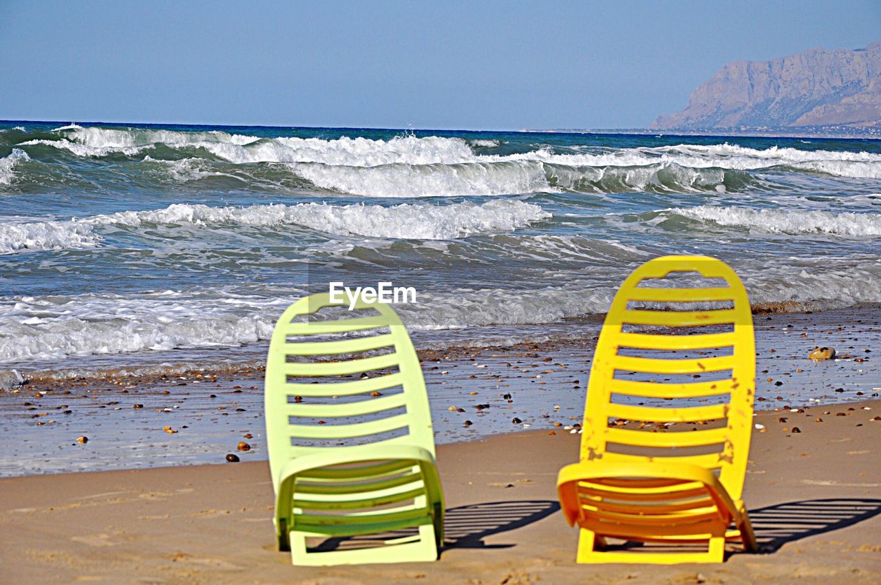 YELLOW DECK CHAIRS ON BEACH AGAINST SKY