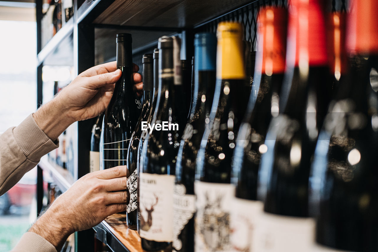 Customer selecting wine bottle from store shelf. a person's hand picking a wine bottle from 