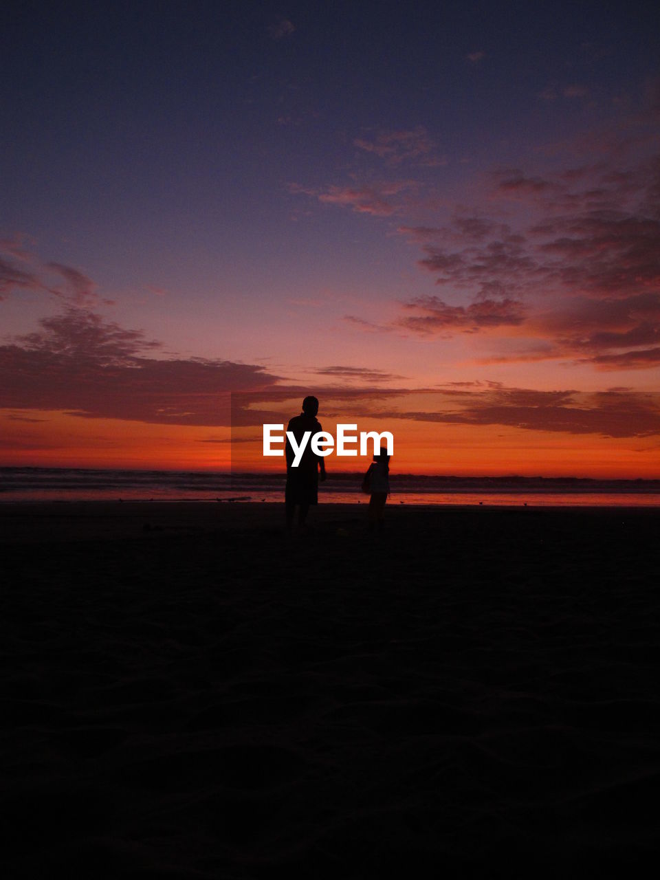 Silhouette of father and daughter playing in the beach while the sun sets 