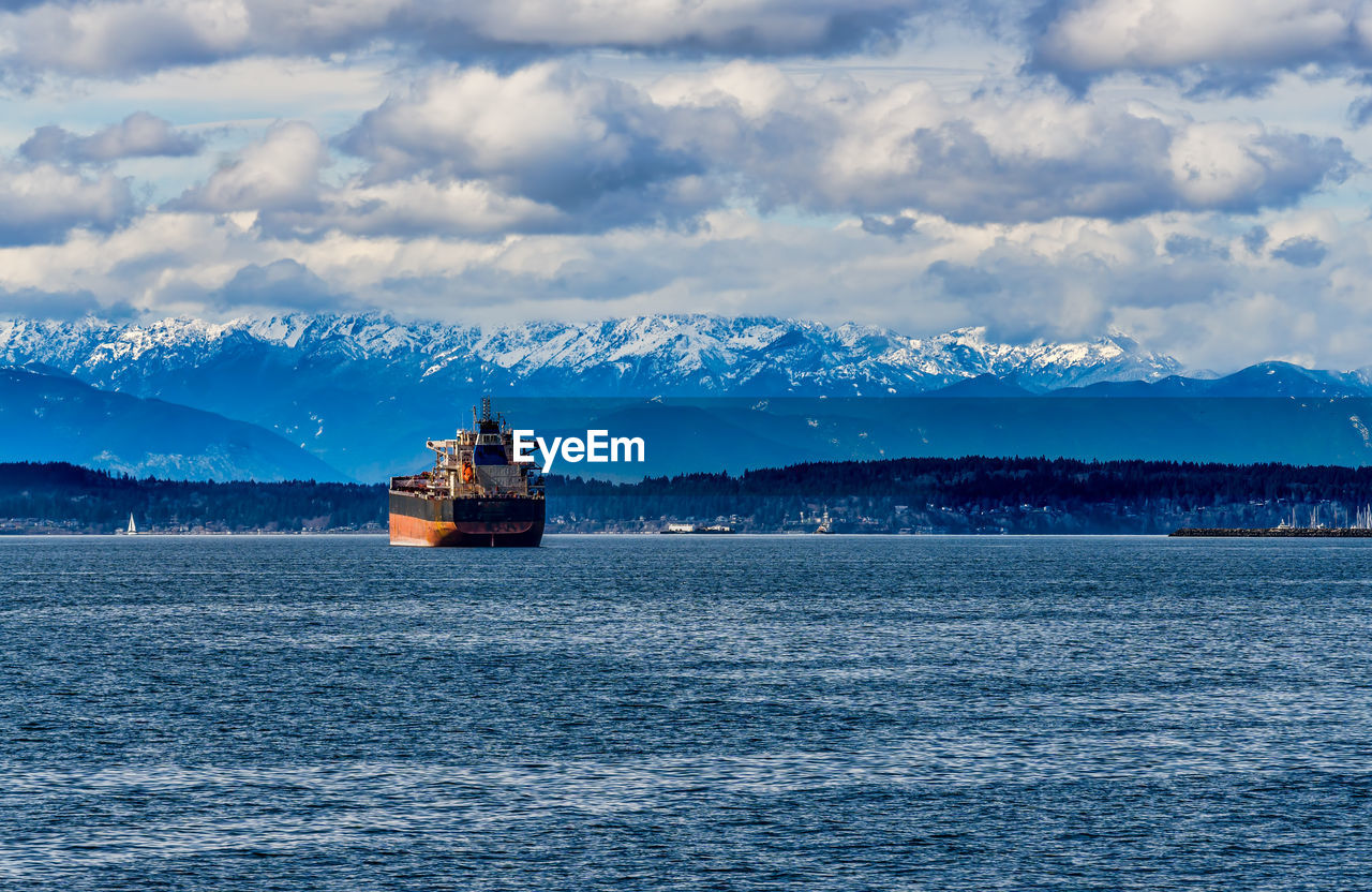 A tanker ship in elliott bay with the olympic mountain range in the distance.