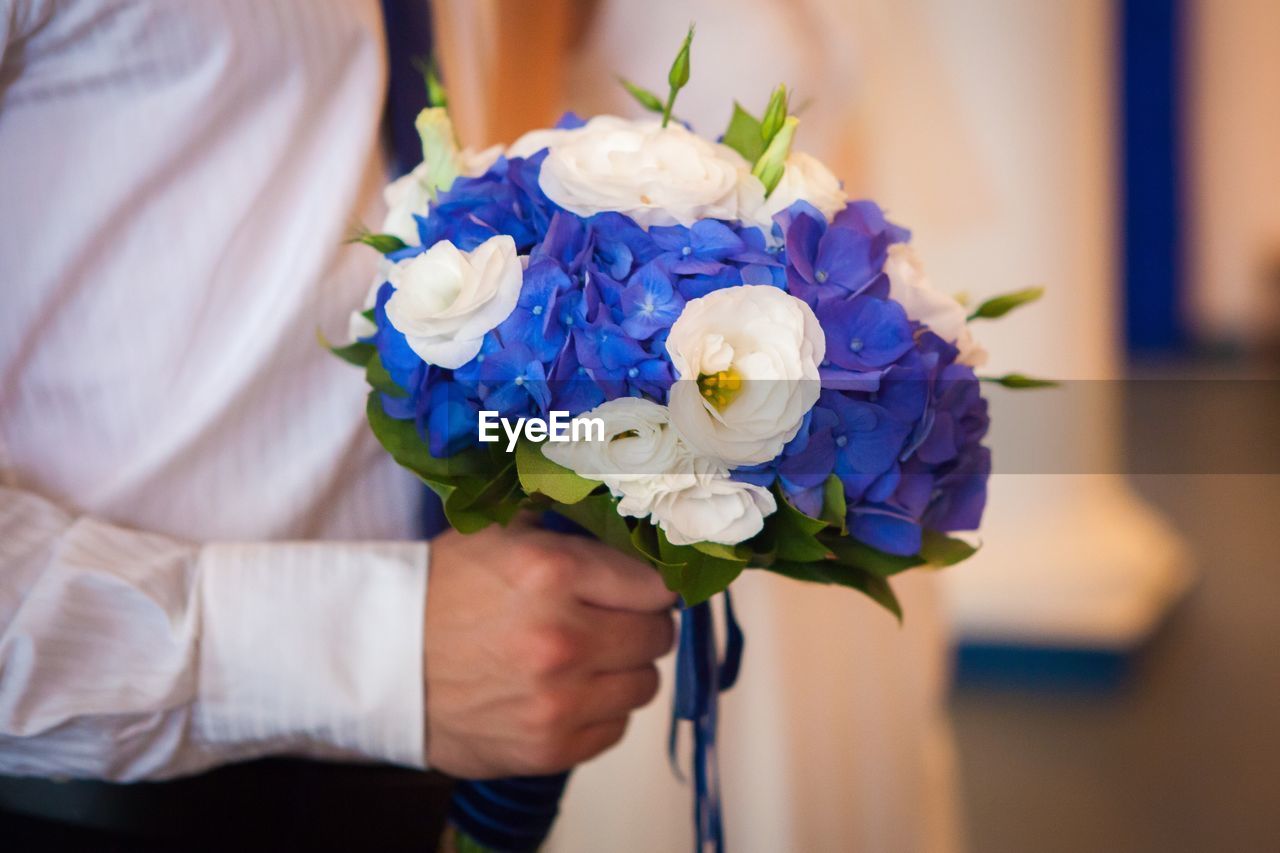 Midsection of groom holding bouquet during wedding