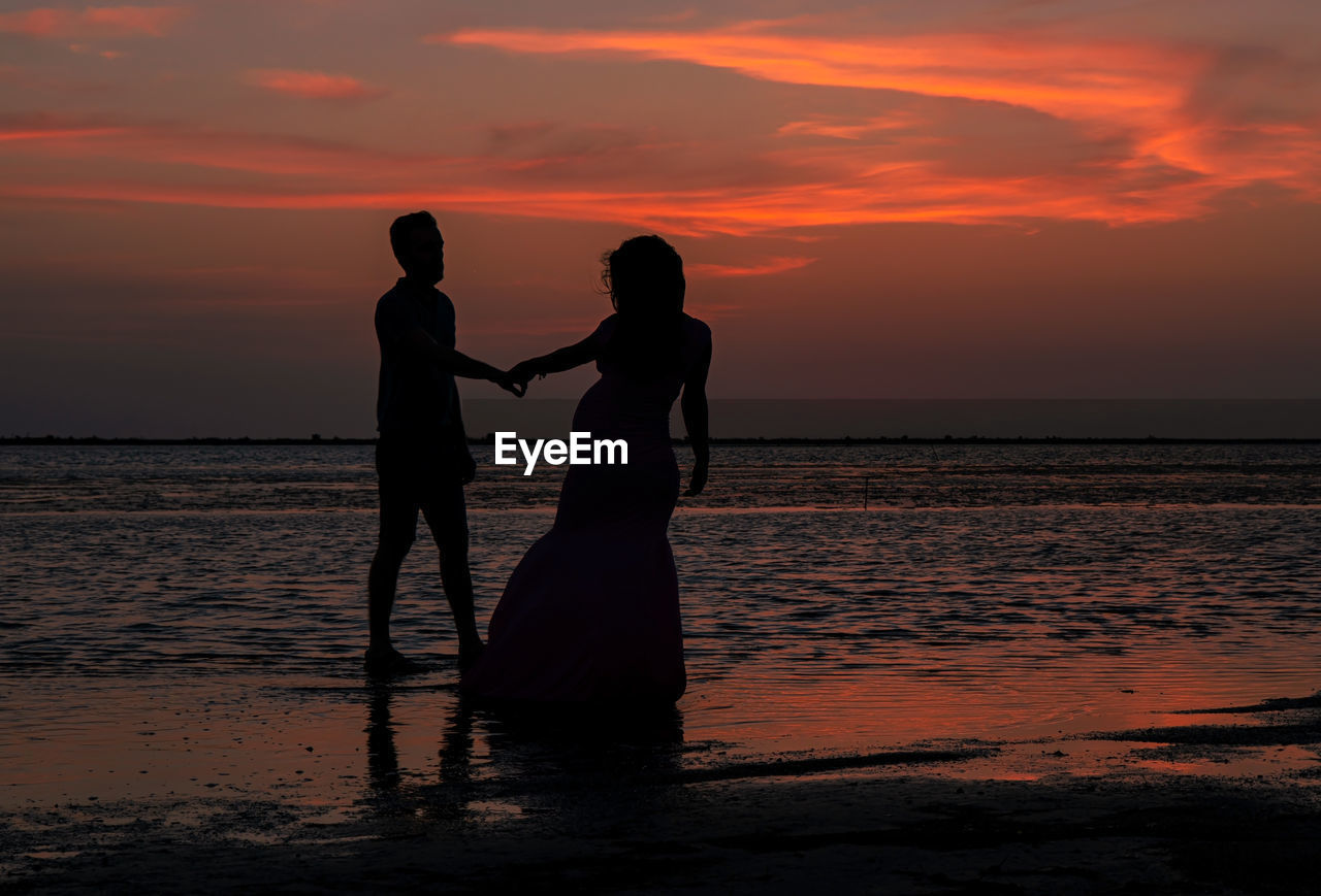 SILHOUETTE COUPLE ON BEACH AGAINST ORANGE SKY