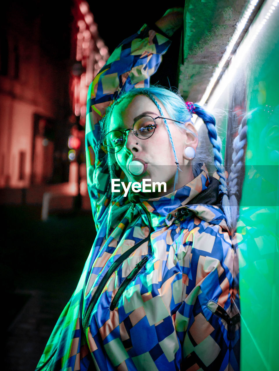 Close-up portrait of young woman blowing bubble gum while standing outdoors at night