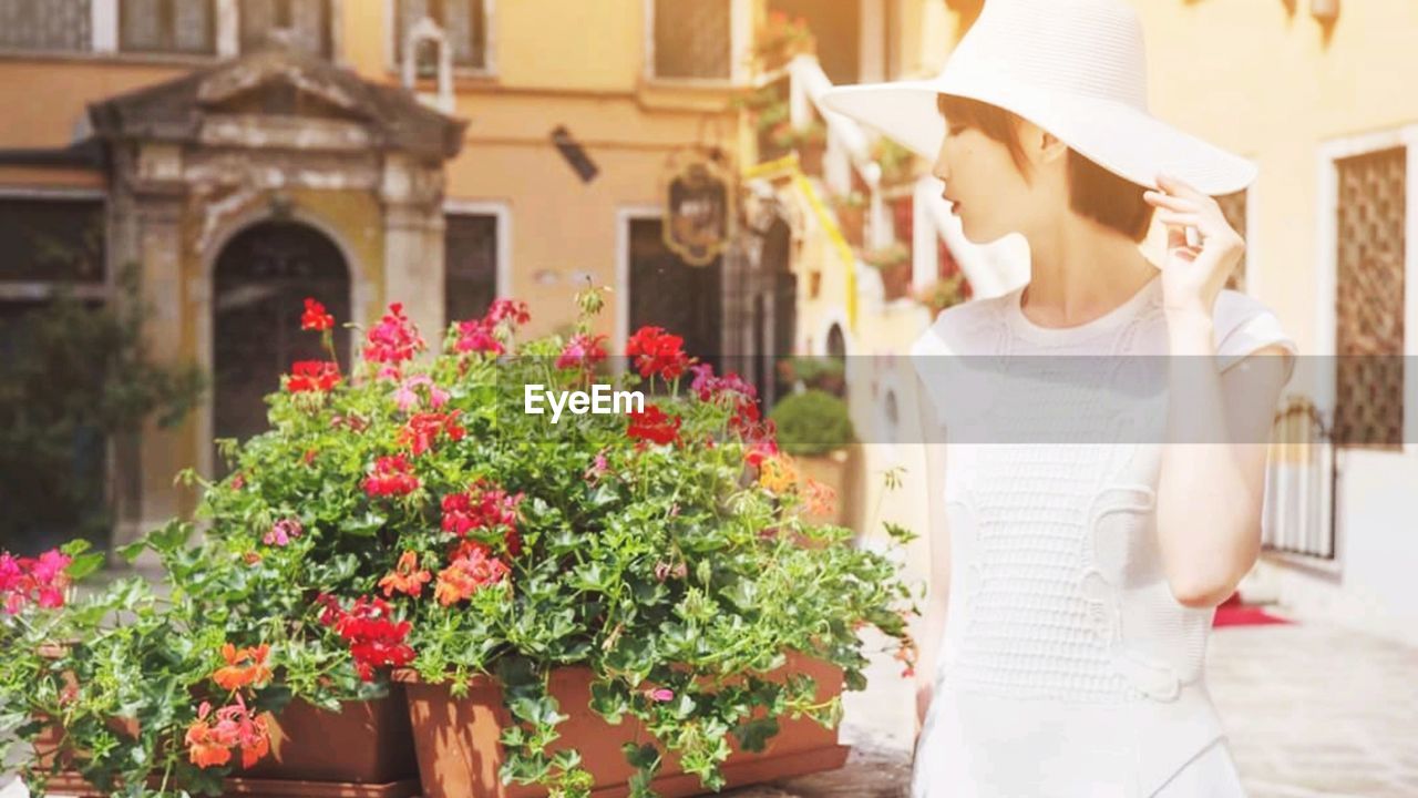 Woman wearing hat while standing by flowering plant