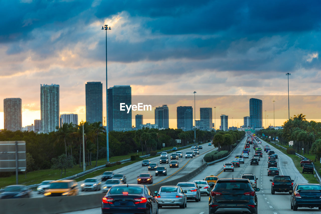 Traffic on road by buildings in city against sky