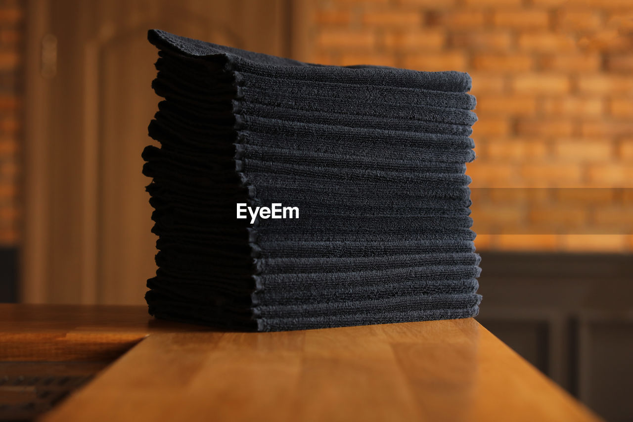 Stacked black bathroom towels on a wooden table and brick wall background. spa salon, barbershop.