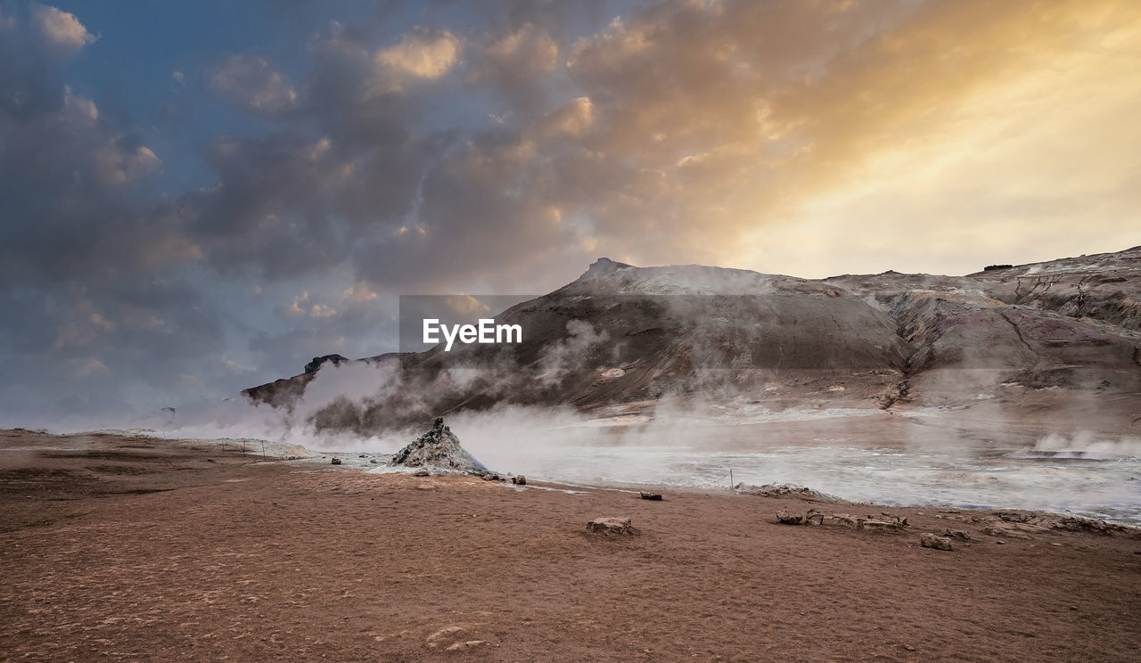 Steam emitting from crater in geothermal area of hverir against sky during sunset