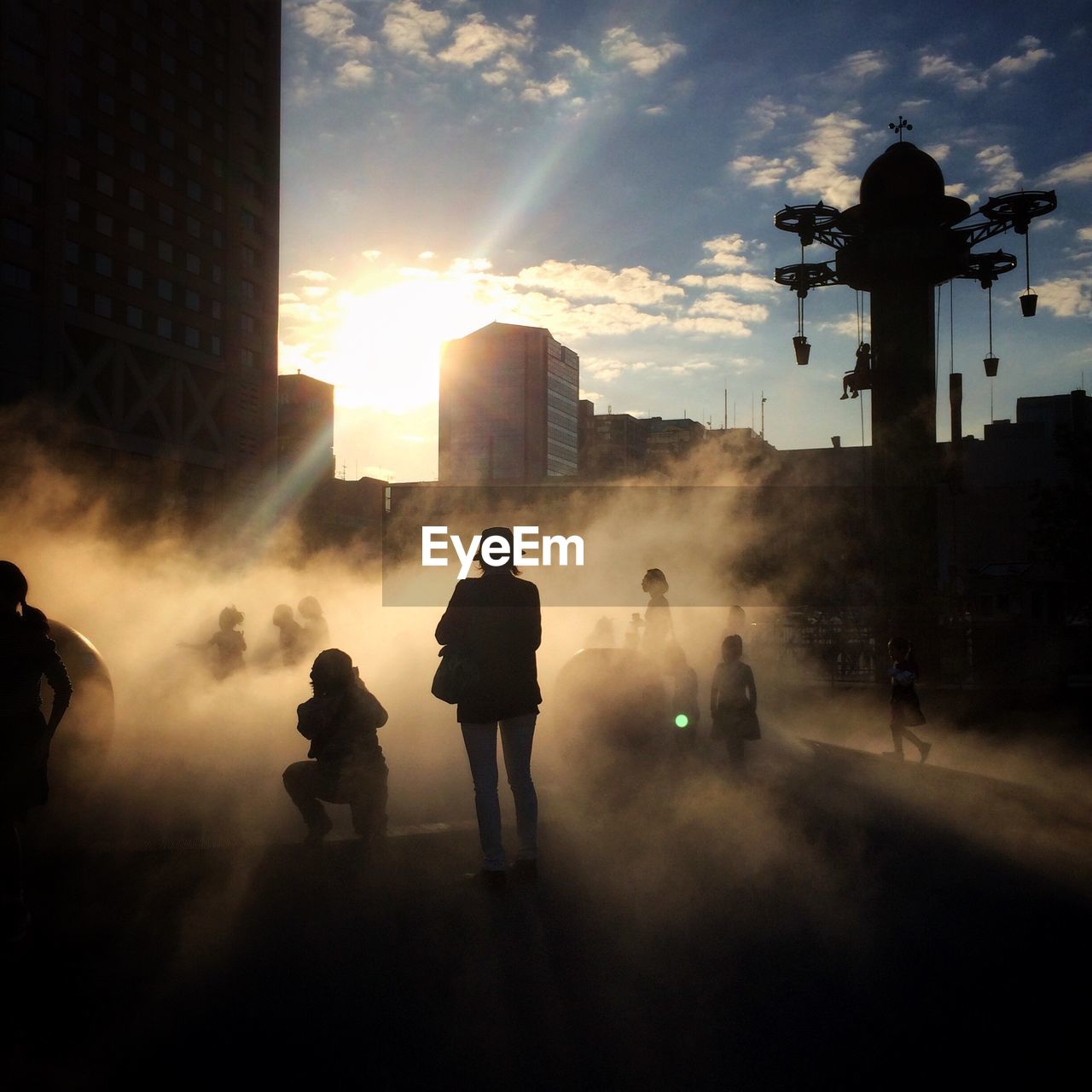 Silhouette people amidst smoke on footpath in city against sky during sunset