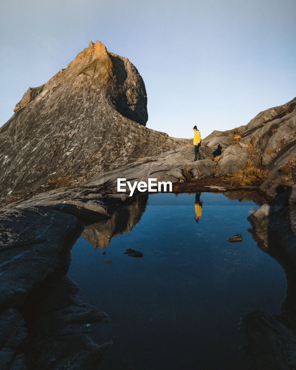 Reflection of woman standing on rock formation in water against sky