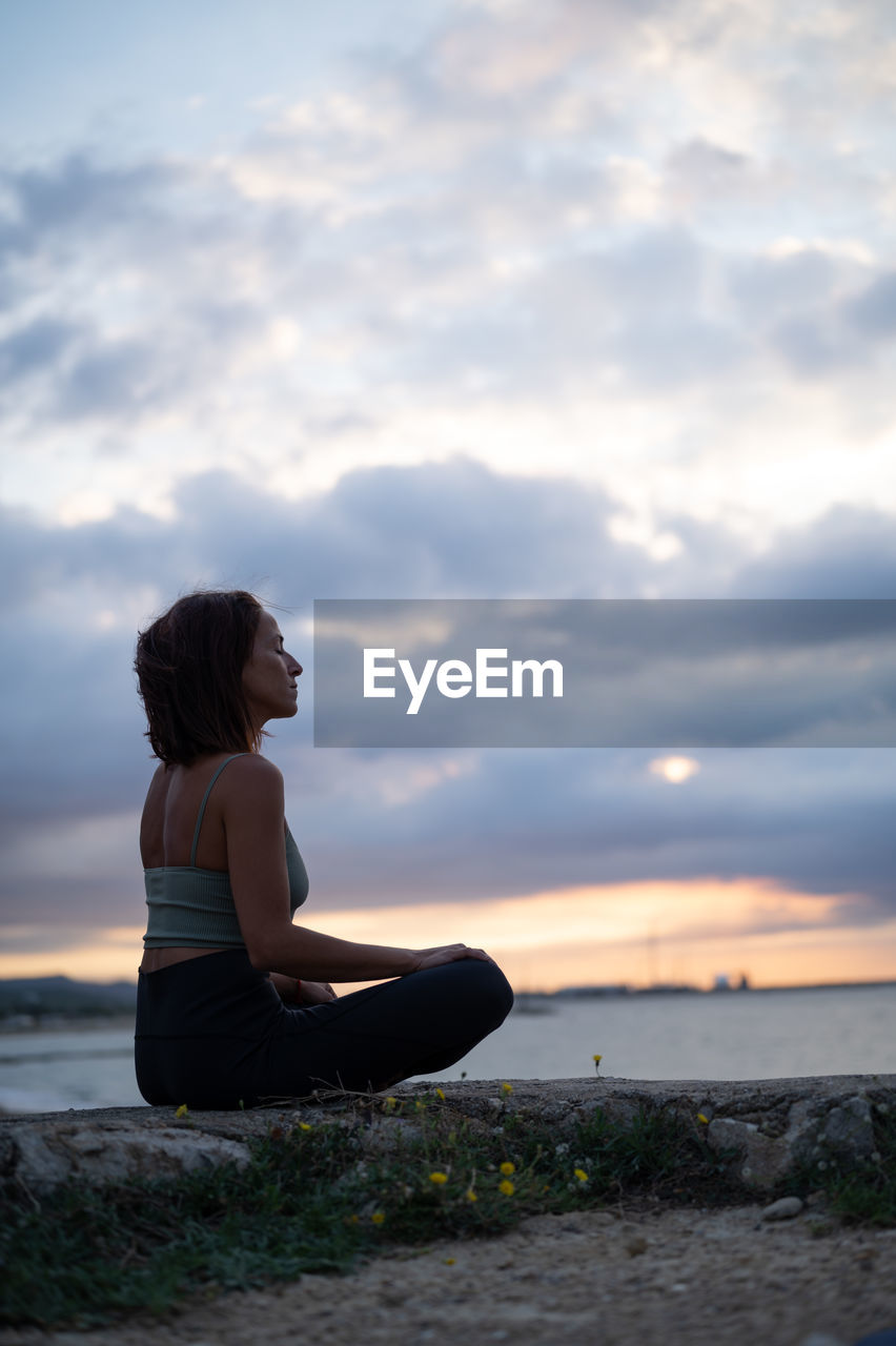 Woman sitting in contemplative mode looking at the sea with cloudy skies.