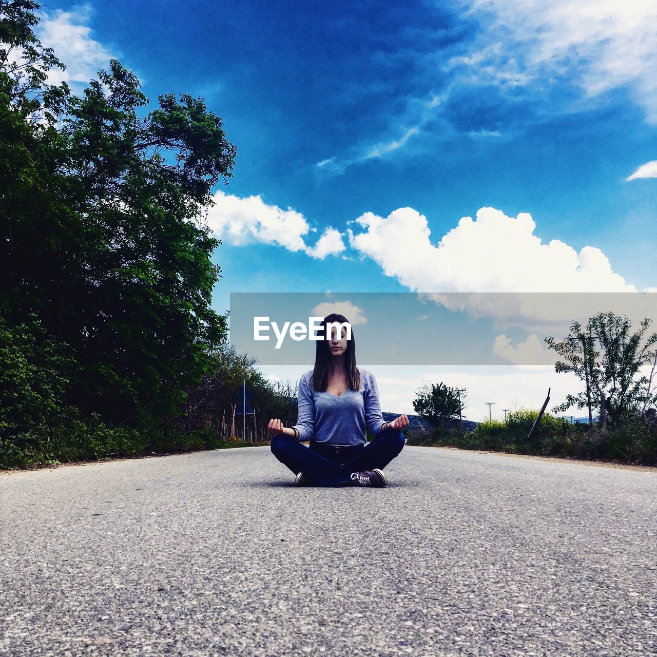 Woman in lotus position sitting on road against sky