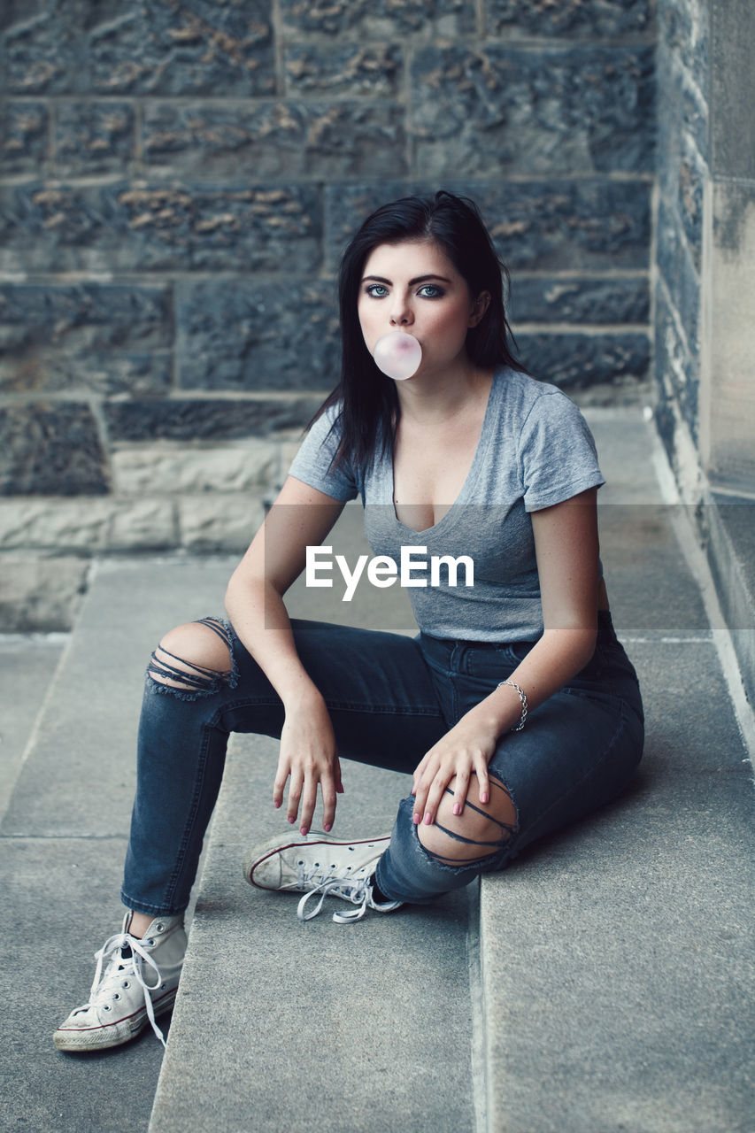 Portrait of young woman blowing gum while sitting on steps