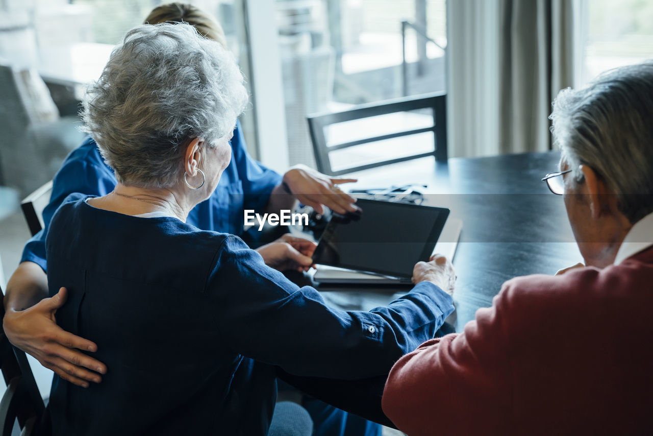 Home caregiver discussing over tablet computer with senior couple while sitting at dining table