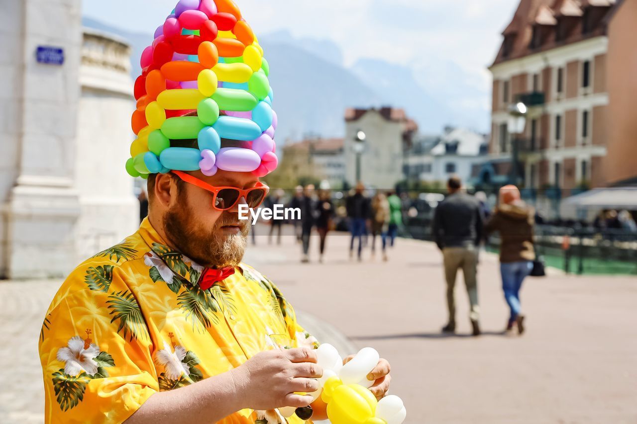 Man wearing colorful balloons on head while standing at street in city