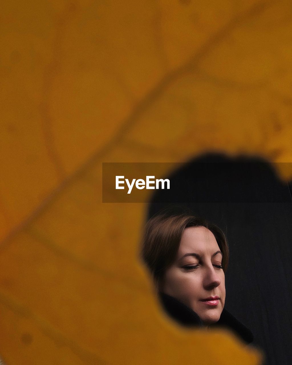 Close-up of woman with eyes closed seen through hole in leaf