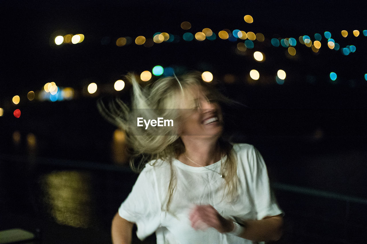 Smiling woman with tousled hair in illuminated city at night