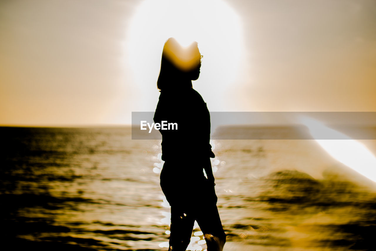 SILHOUETTE MAN STANDING ON BEACH DURING SUNSET