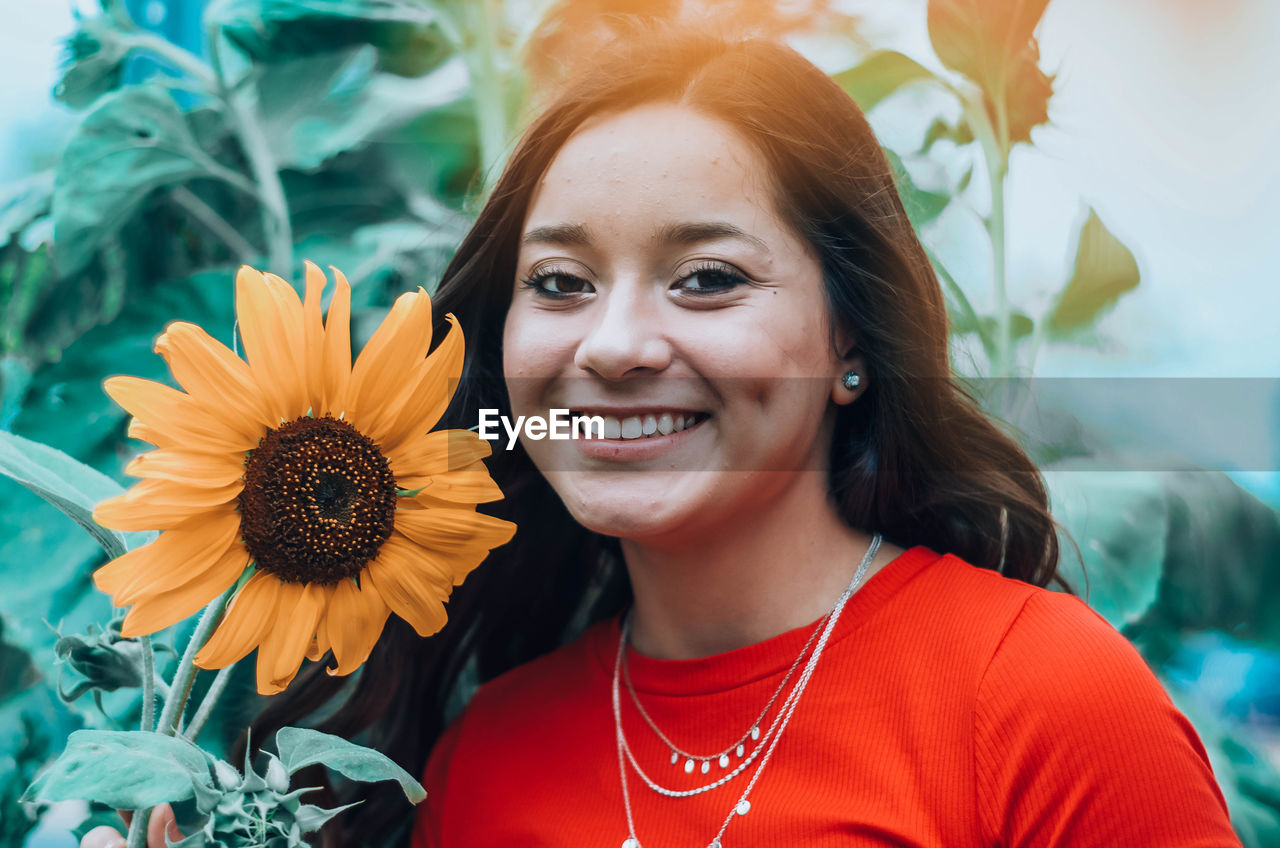 Portrait of smiling woman holding sunflower outdoors