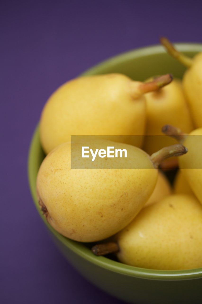 Pears in a green bowl on purple background