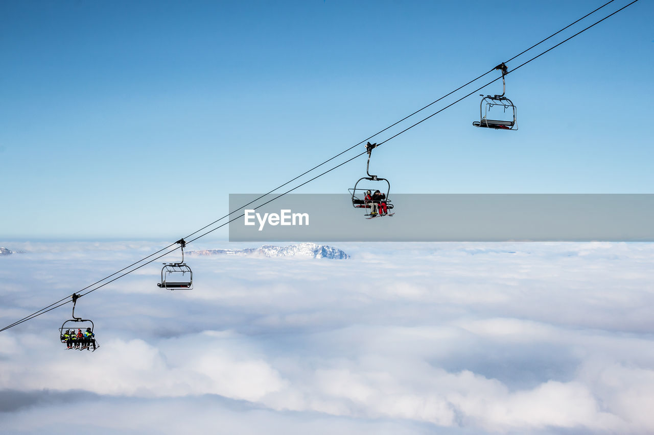 Ski lifts above cloudscape against clear sky