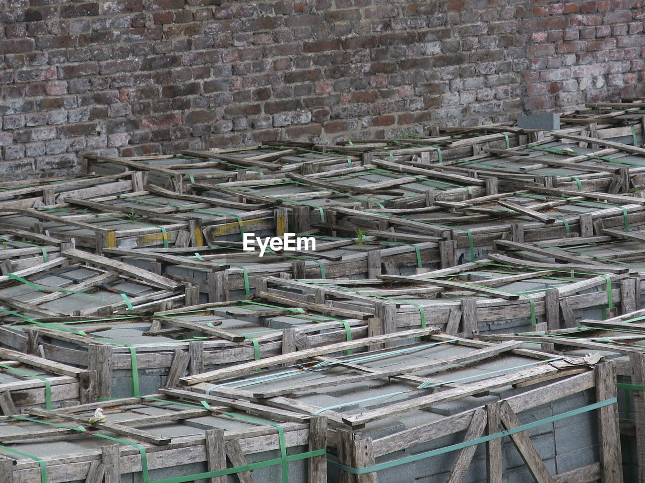 Collection of woorden crates filled with gray bricks against a red brick wall