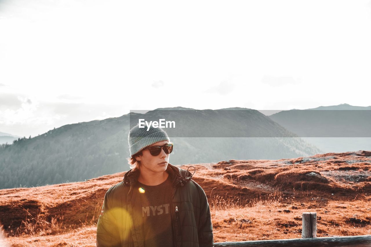 YOUNG MAN STANDING ON MOUNTAINS AGAINST SKY