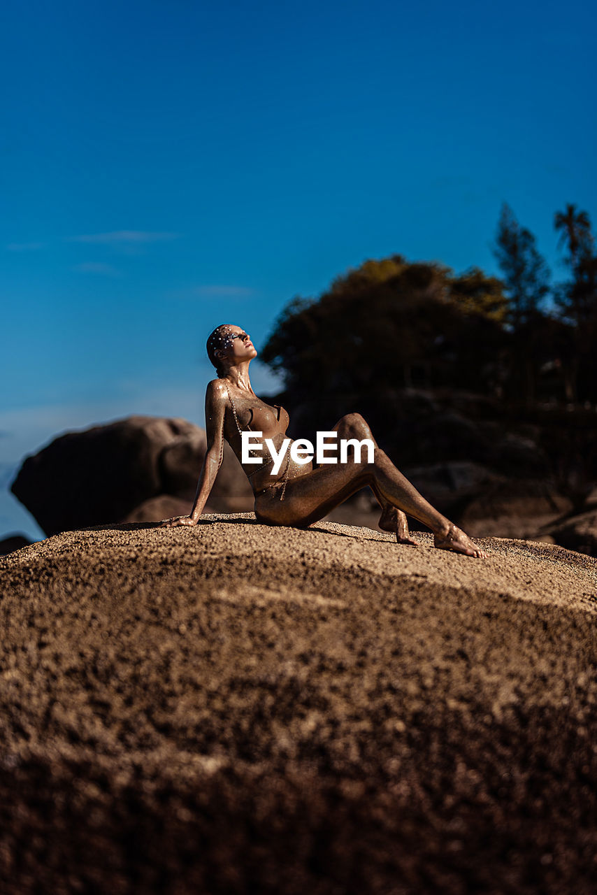 Young woman with golden skin sits on a stone