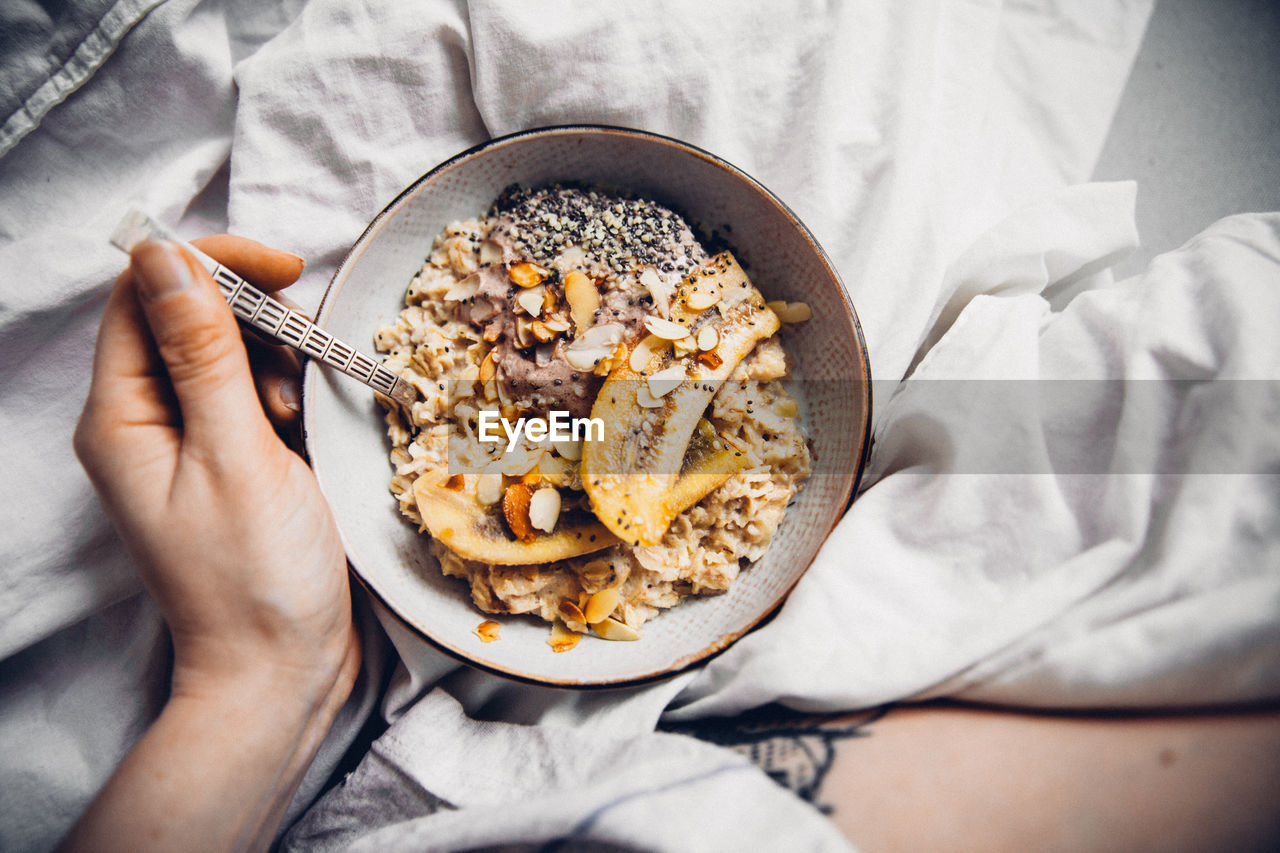 Close-up of hand eating granola in bowl on bed