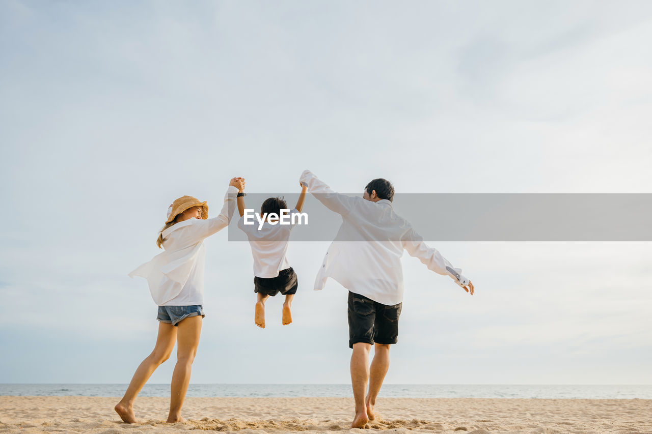 rear view of woman standing at beach against sky