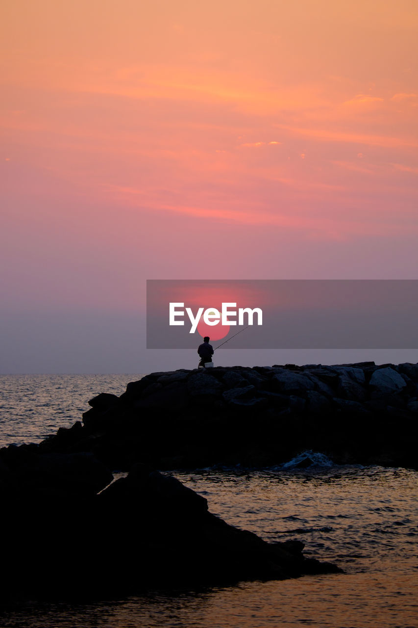 Silhouette man fishing against orange sky during sunset