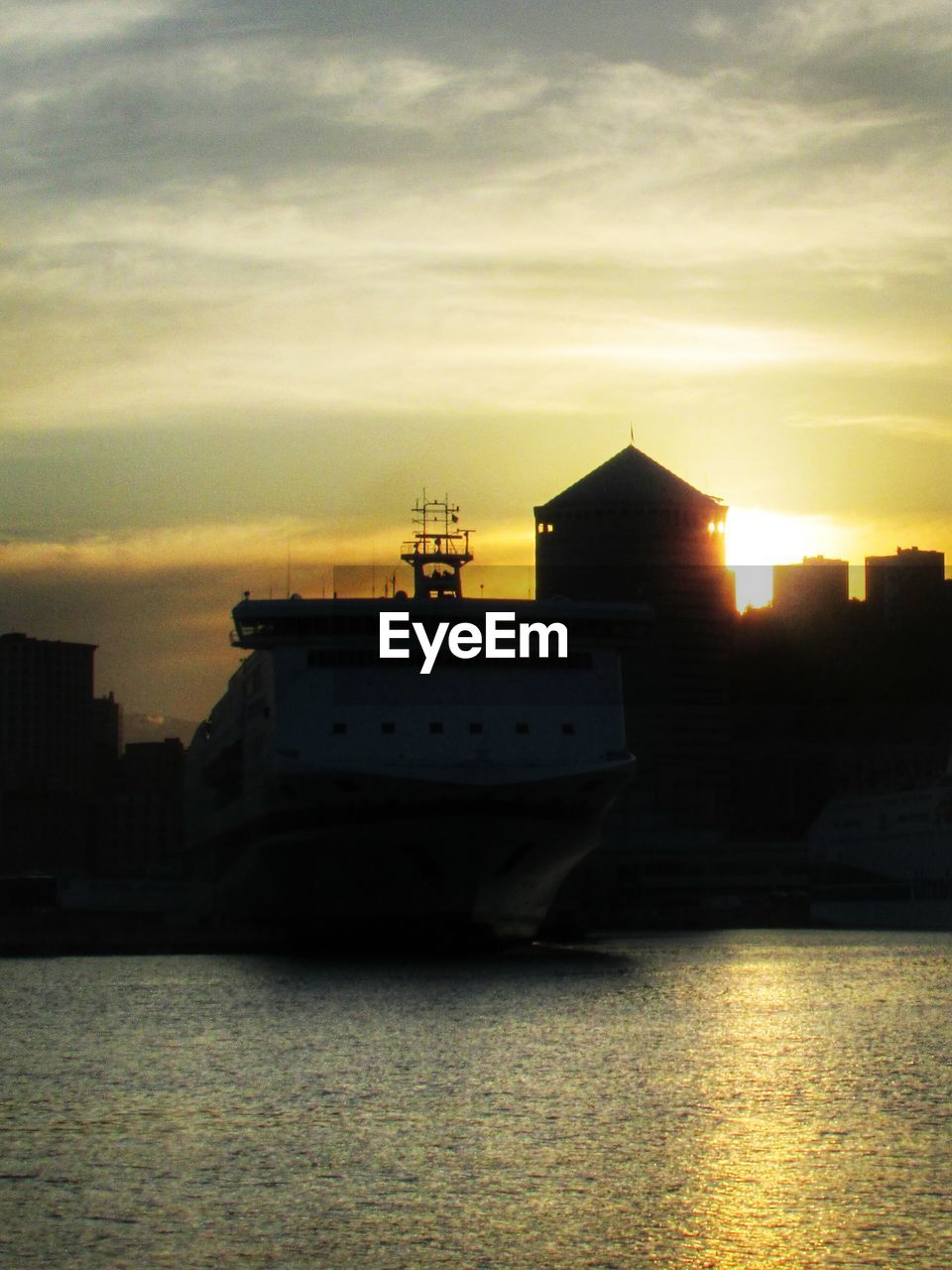 Cruise ship on water against silhouette buildings during sunset