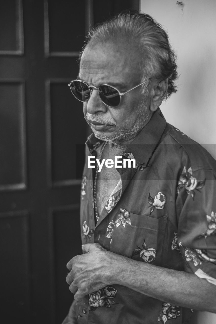 MAN WEARING SUNGLASSES LOOKING AWAY WHILE STANDING ON WALL