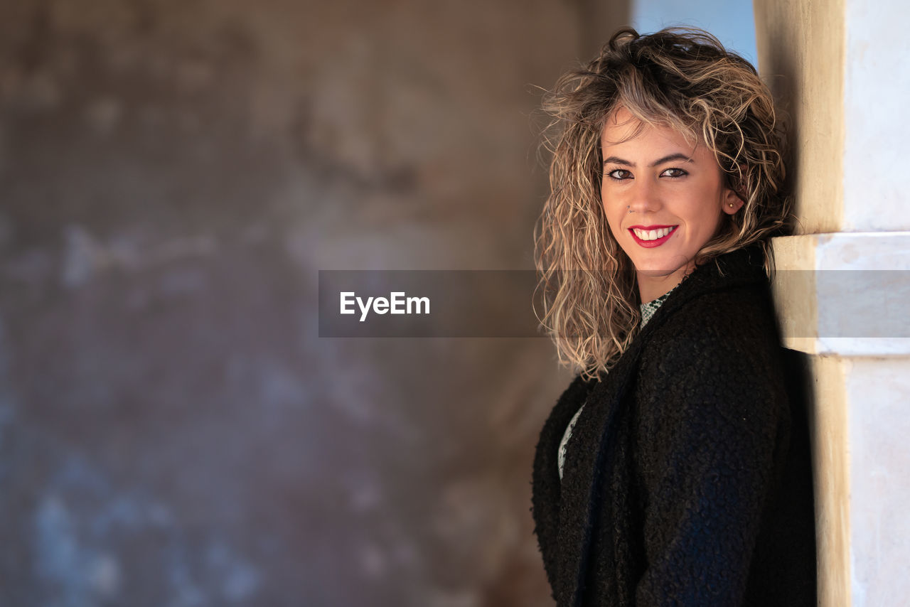 Portrait of smiling young woman standing by wall