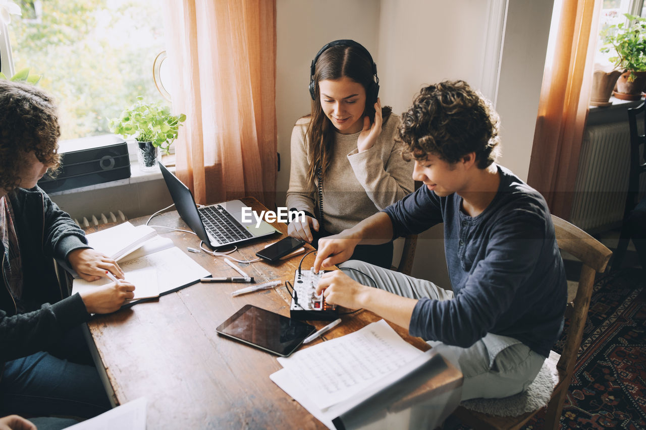 High angle view of friends using sound mixer while teenage boy studying at table in room