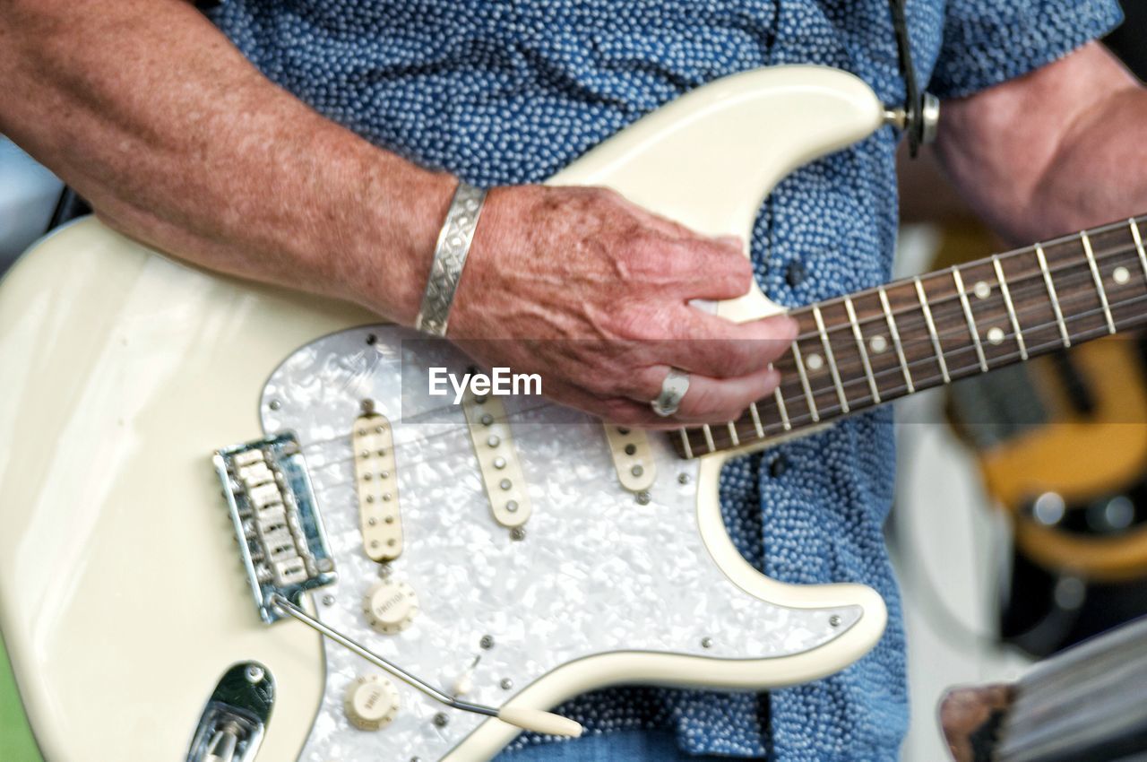 MIDSECTION OF MAN PLAYING GUITAR ON CARPET