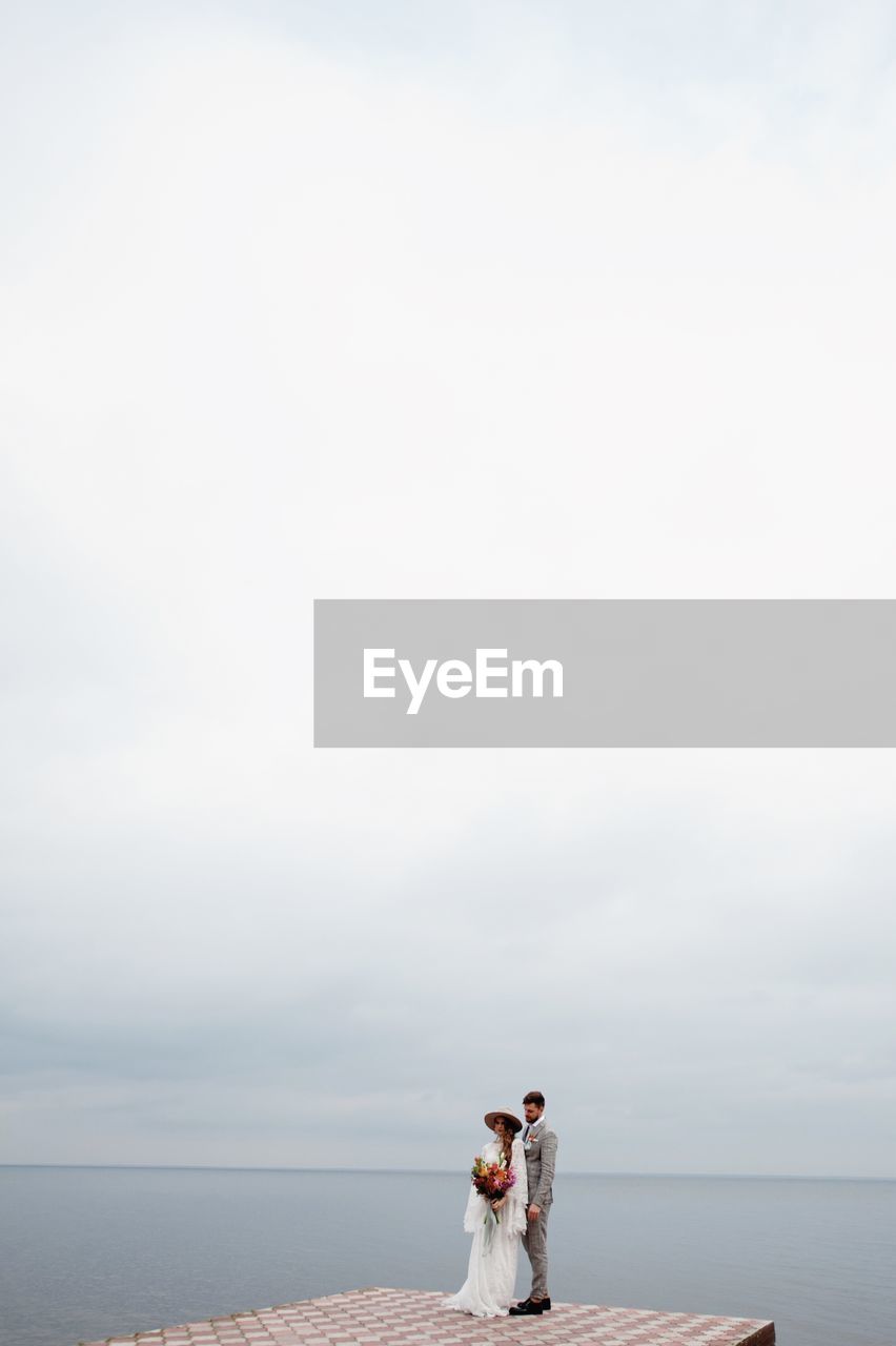 Bride and bridegroom standing on pier in sea during wedding ceremony