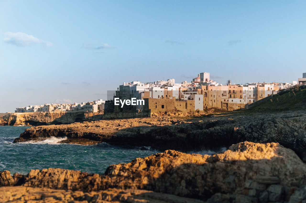 Buildings by sea against clear blue sky